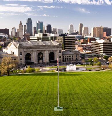 A view of the city from above shows a grassy field and buildings.