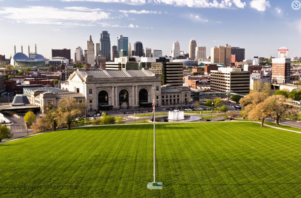 A view of the city from above shows a grassy field and buildings.