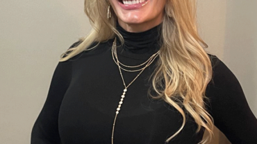A woman in black shirt and necklace smiling for the camera.