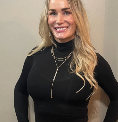 A woman in black shirt and necklace smiling for the camera.